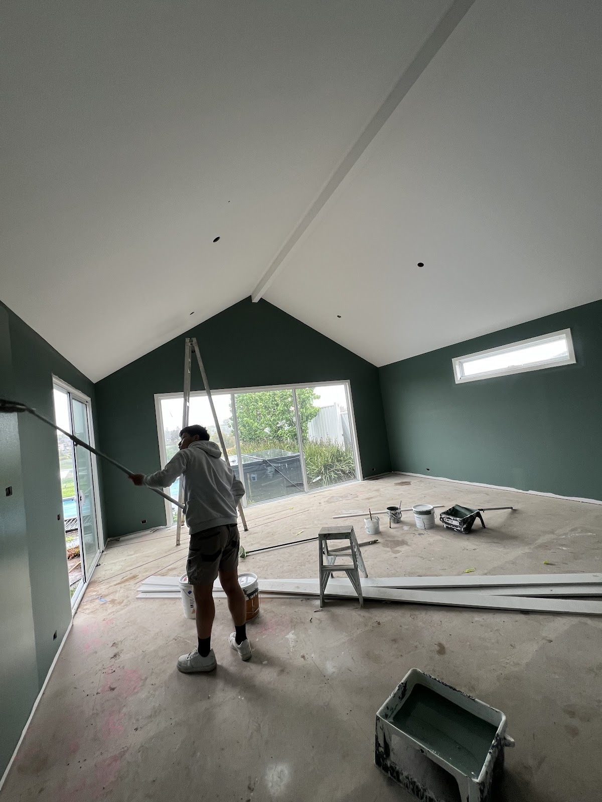 Painter rolling a deep green feature wall in a living room with a raked ceiling