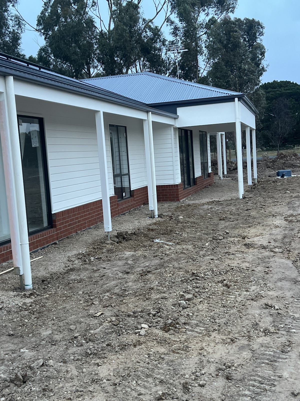 New home exterior with white weatherboards and posts above a red brick base