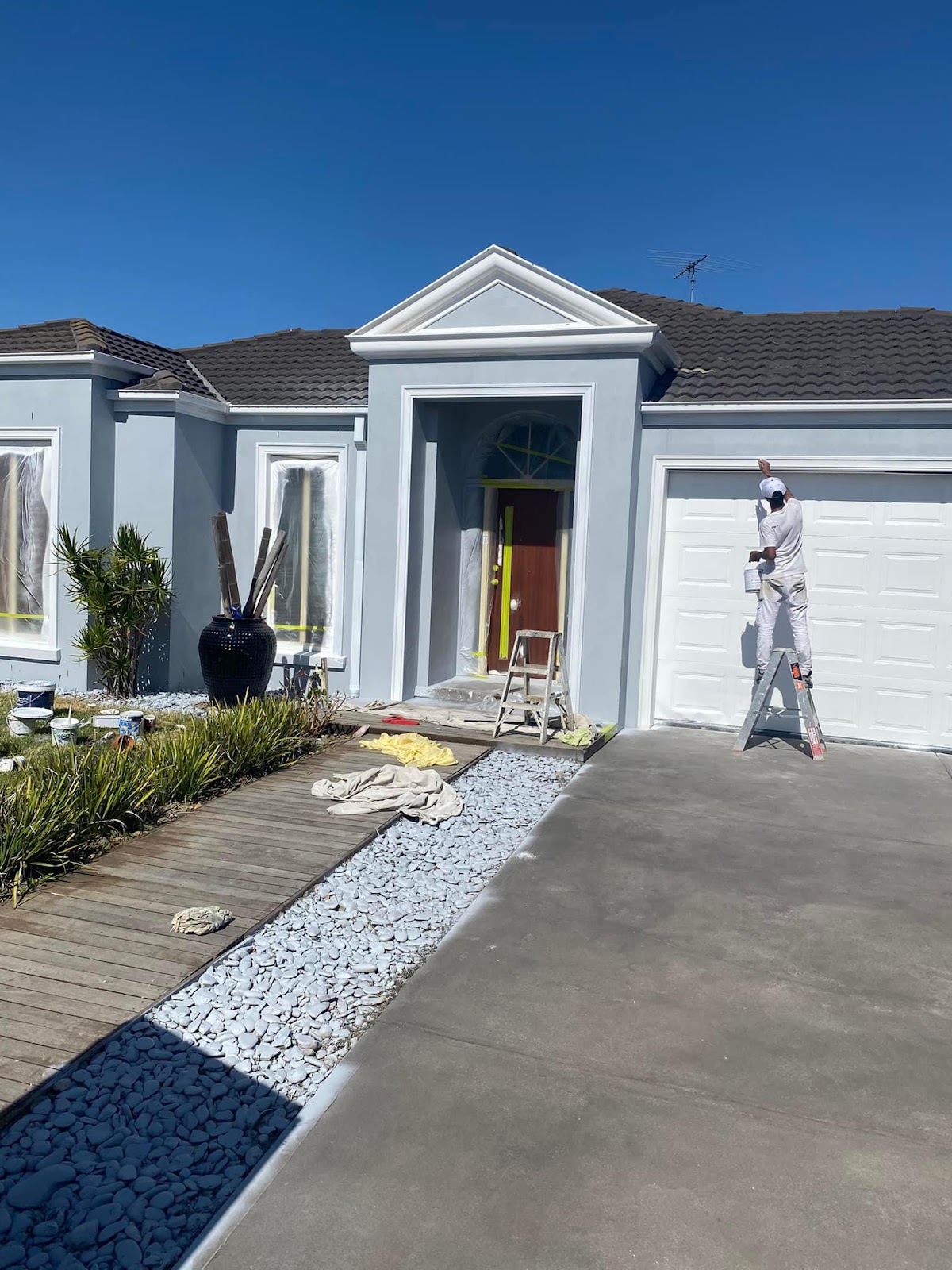 Rendered house front freshly painted grey blue with white trims, a painter on a ladder by the garage