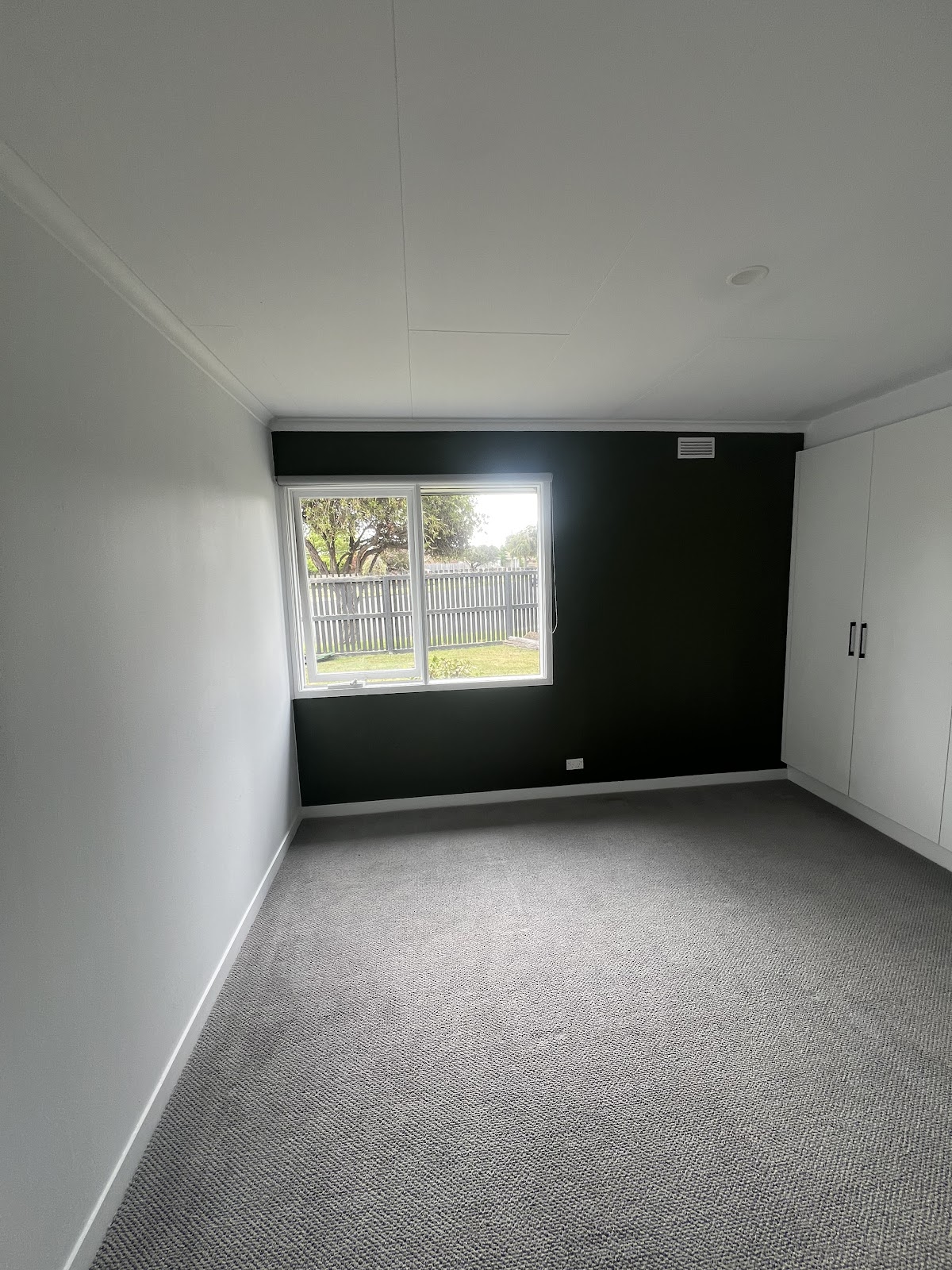 Finished bedroom with a black feature wall, white walls and new carpet