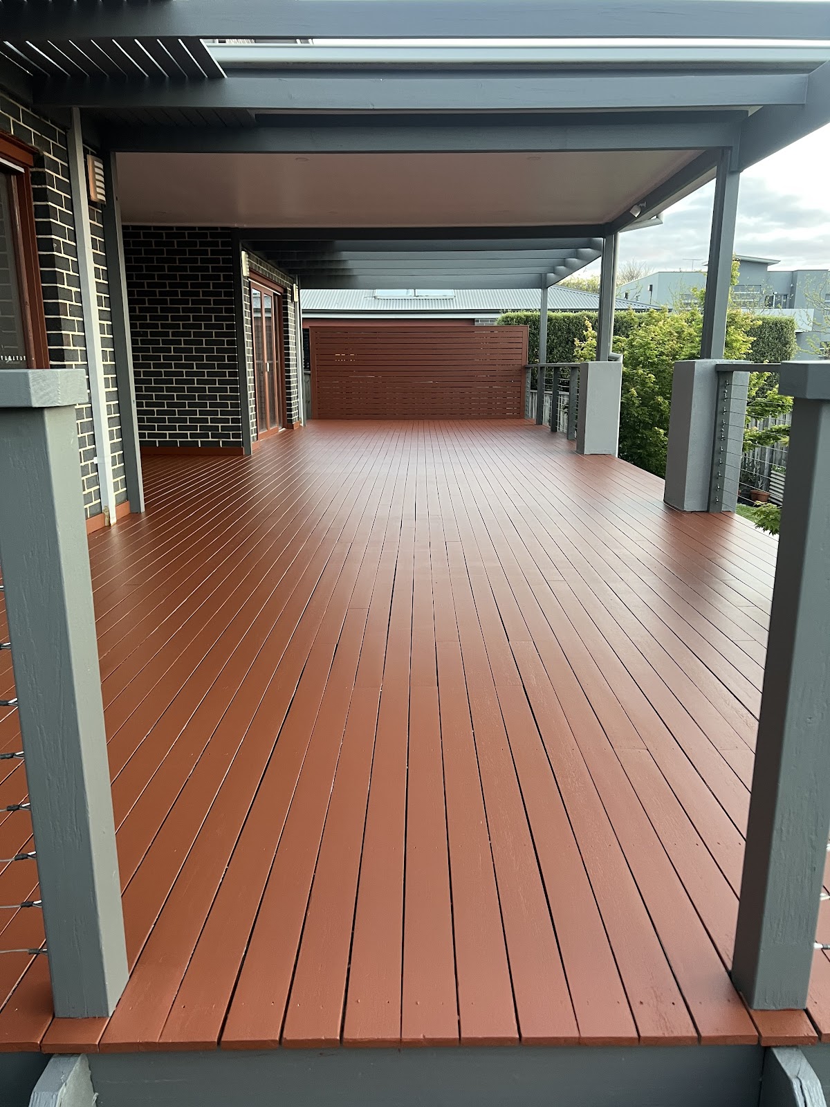 Long timber deck stained a warm red brown under a pergola
